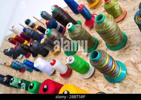 Colorful thread reels on wooden wall set up for sewing machine, textile industry factory concept Stock Photo