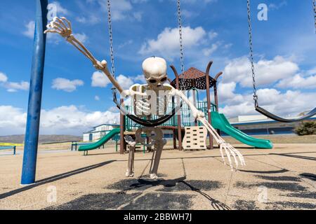 Skeleton playing superman on a child's swing in an empty park Stock Photo