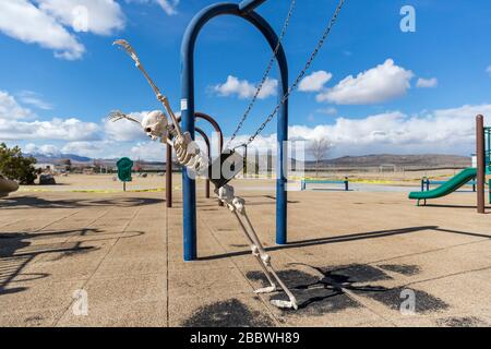 Skeleton playing superman on a child's swing in an empty park Stock Photo