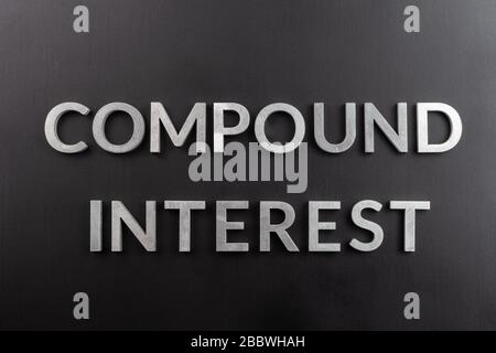 the words compound interest laid with silver metal letters on matte black surface in flat lay composition, directly above view Stock Photo
