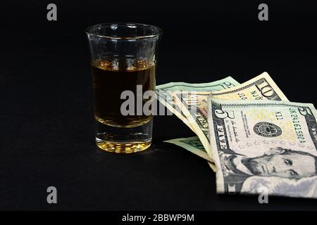close up of folded American money and shot of whiskey on black Stock Photo