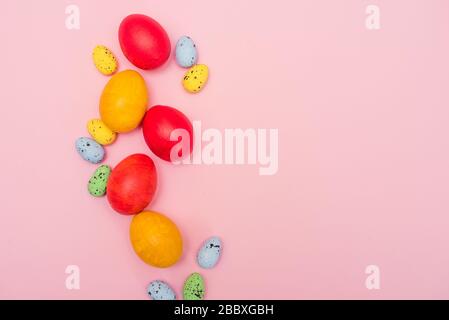 Easter colored eggs on a pink background. Red and yellow chicken eggs with pastel quail eggs. Easter card. Copy space. Stock Photo