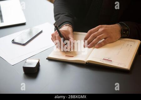 businessman working on laptop in office taking notes by window black table with notebook papers phone Stock Photo