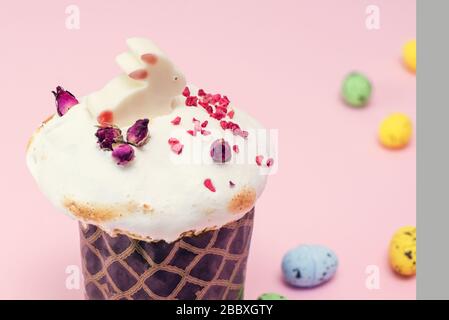 Easter cake decorated with cream in the form of grass and a white chocolate rabbit figurine on a pink background next to painted quail pastel eggs. Easter gift card. Stock Photo