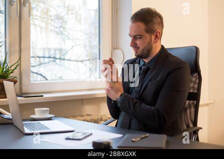 businessman working on laptop in office wrist pain by window black table with notebook papers phone Stock Photo