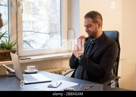 businessman working on laptop in office wrist pain by window black table with notebook papers phone Stock Photo