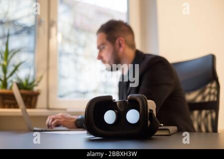 businessman working in office virtual reality goggles waiting for him by window black table with notebook papers phone VR Stock Photo