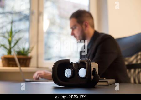 businessman working in office virtual reality goggles waiting for him by window black table with notebook papers phone VR Stock Photo