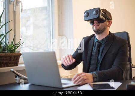 businessman finishes his work and taking virtual reality goggles on by window black table with notebook papers phone VR Stock Photo