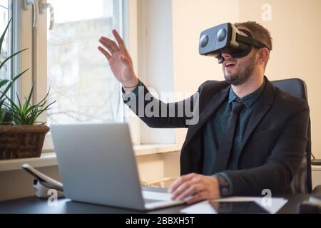 businessman finishes his work and taking virtual reality goggles on by window black table with notebook papers phone VR Stock Photo