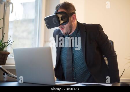 businessman finishes his work and taking virtual reality goggles on by window black table with notebook papers phone VR Stock Photo