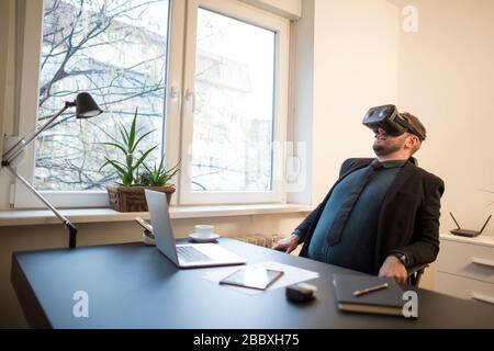 businessman finishes his work and taking virtual reality goggles on by window black table with notebook papers phone VR Stock Photo