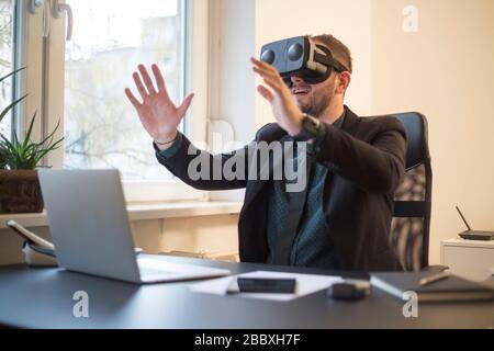 businessman finishes his work and taking virtual reality goggles on by window black table with notebook papers phone VR Stock Photo