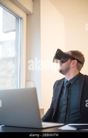 businessman finishes his work and taking virtual reality goggles on by window black table with notebook papers phone VR Stock Photo