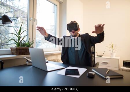businessman finishes his work and taking virtual reality goggles on by window black table with notebook papers phone VR Stock Photo