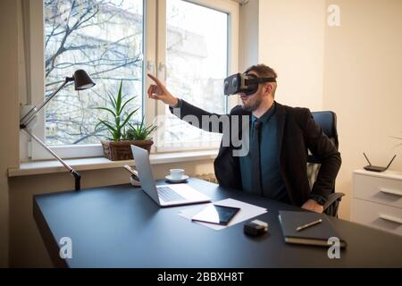 businessman finishes his work and taking virtual reality goggles on by window black table with notebook papers phone VR Stock Photo