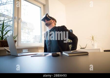 businessman finishes his work and taking virtual reality goggles on by window black table with notebook papers phone VR Stock Photo