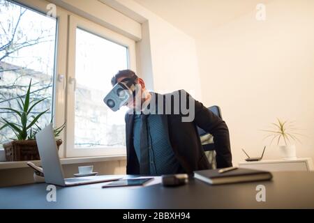 businessman finishes his work and taking virtual reality goggles on by window black table with notebook papers phone VR Stock Photo