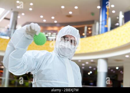man in coverall disposable anti-epidemic antibacterial isolation suit suspiciously holds in his hand a rubber ball resembling a macro photo of a virus Stock Photo