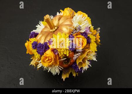 Small pumpkin decorated with yellow and blue flowers as a gift on a black background. Stock Photo