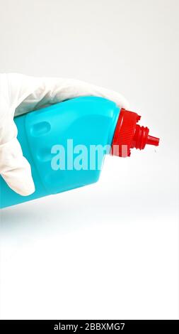 Blue plastic bottle with a red cap in hand in a rubber white glove on a white background.Liquid for cleaning and disinfection of rooms and houses. Stock Photo