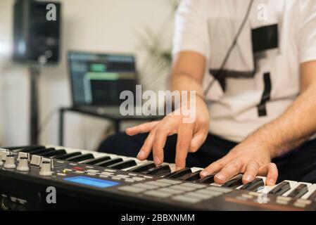 Close up of professional musician recording midi keyboard in digital studio at home. He is surrounded with instruments and midi controller. Music prod Stock Photo