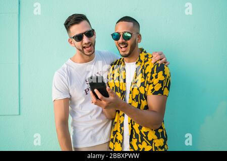 Portrait of happy gay couple spending time together while using mobile phone. Lgbt and love concept. Stock Photo