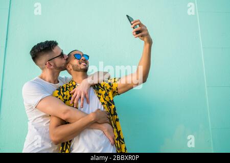 Portrait of happy gay couple spending time together and taking a selfie with mobile phone. Lgbt and love concept. Stock Photo