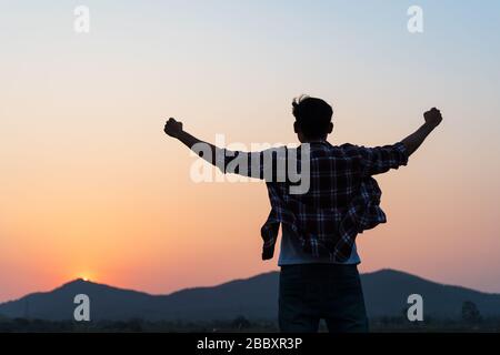 Man with fist in the air during sunset sunrise mountain in background. Stand strong. Feeling motivated, freedom, strength and courage concept. Stock Photo