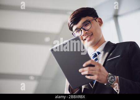 A asian handsome young businessman using his tablet and standing on the escalator. Business concept. Stock Photo