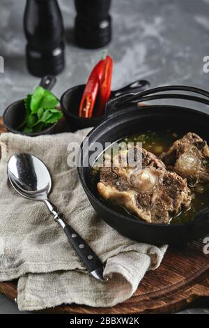 Shurpa soup in a cast-iron pot on the table on a gray background. Traditional oriental cuisine. Stock Photo