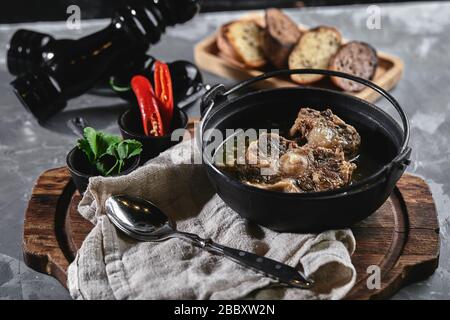 Shurpa soup in a cast-iron pot on the table on a gray background. Traditional oriental cuisine. Stock Photo