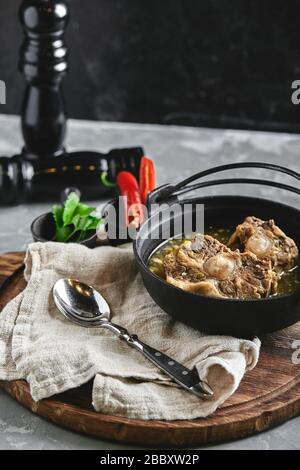 Shurpa soup in a cast-iron pot on the table on a gray background. Traditional oriental cuisine. Stock Photo