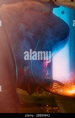 Welder uses welding machine to make sparks during manufacture of metal construction. Stock Photo