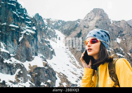 Beautiful young woman hold in hands mobile phone, person type message on smartphone, relax tourist travels planning trip in rock snow mountain Stock Photo