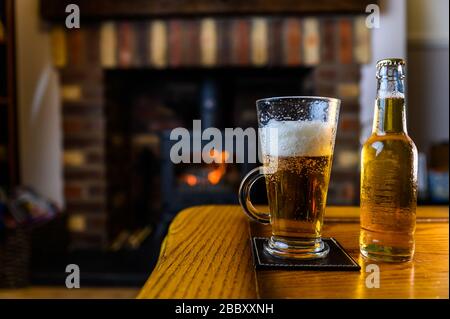 Beer poured into glass on oak table with log burner fire on background at home