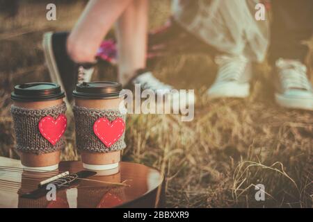 Romantic couple hugging while having picnic in sunset light. Coffee cup cozy knitted sleeve with felt red heart. Stock Photo