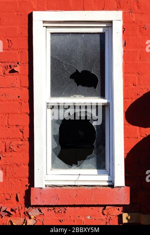A white painted window sash with broken windows against a red brick wall with peeling paint. Stock Photo