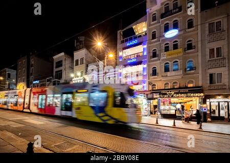 A tram is blurred as it speeds through the street past cafes and shops near the Blue Mosque in the Sultanahmet district of Istanbul, turkey at night. Stock Photo