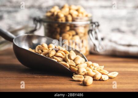 Roasted salted peanuts. Crispy nuts in metal scoop on wooden table. Stock Photo