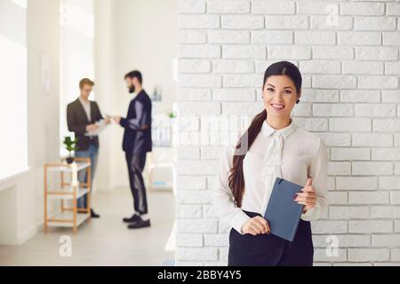 Hispanic latin businesswoman smiling while standing in a white office against a white wall. Stock Photo