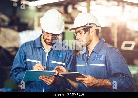 Engineer audit worker working team together with safety uniform and white helmet to work in industry factory handle tablet and checklist. Stock Photo