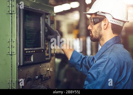 worker operate CNC machine with G-Code monitor, high skill labor work industry with safety clothes. Stock Photo