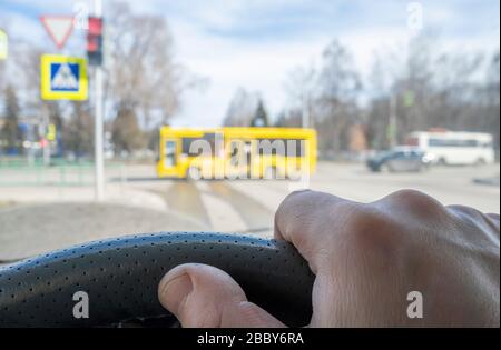 the driver hand on the steering wheel of a car located in front of a red prohibiting traffic light, pedestrian crosswalk, and cars that the driver giv Stock Photo