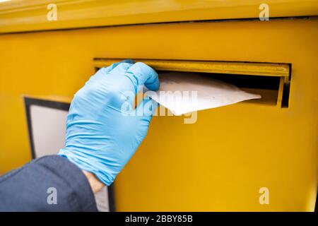 Man Inserting Letter In Mailbox Wearing Gloves To Protect From Coronavirus Stock Photo
