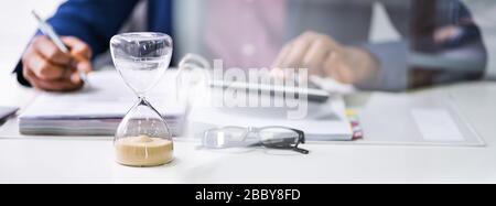 Hourglass In Front Of Businessperson Calculating Invoice Stock Photo