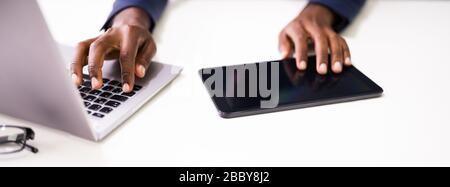 Businessperson's Hands Using Tablet And Laptop On Desk Stock Photo