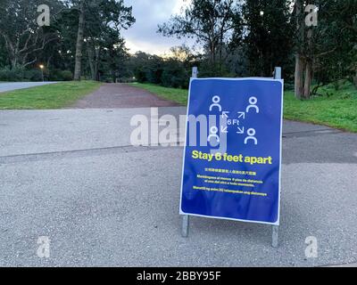Coronavirus COVID-19 social distancing signboard in public park in front of dirt walking path trail Stock Photo