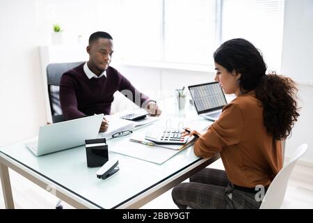 Close-up Of Two Businesspeople Calculating Financial Statement At Desk Stock Photo