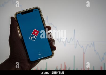 Domino s pizza mobile app held against a white stock trading chart going down in value Stock Photo